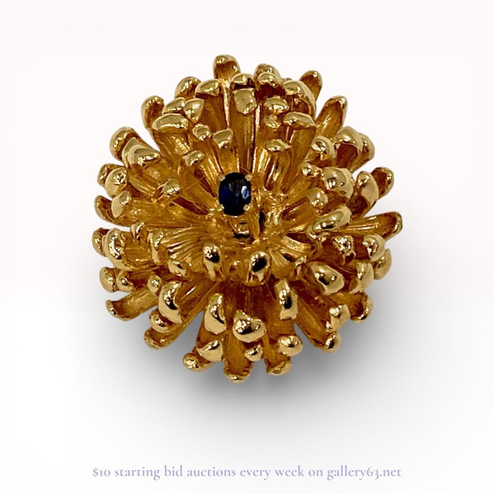 Description
Vintage floral-form pendant by maker LEI, designed in a textured sea anemone or chrysanthemum style. The piece is crafted from gold-plated sterling silver featuring numerous radiating curved petals and a central oval-cut dark blue sapphire in a prong setting. A threaded assembly hole is visible beneath the center stone, and the reverse is fitted with a fixed pendant bail. The reverse is stamped with a 925 fineness mark and the maker mark LEI.
Center stone: approximately 4mm x 3mm.