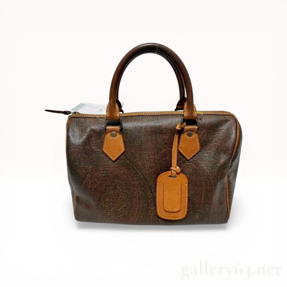 Description
Etro Boston bag featuring the signature multicolored paisley pattern on coated canvas with tan leather trim. The structured design includes dual rolled top handles, a full-length top zipper closure, and an interior zippered side pocket. An interior leather patch and the metal zipper pull are marked with the Etro Milano name and Pegasus logo.
Width: Approximately 12 inches.