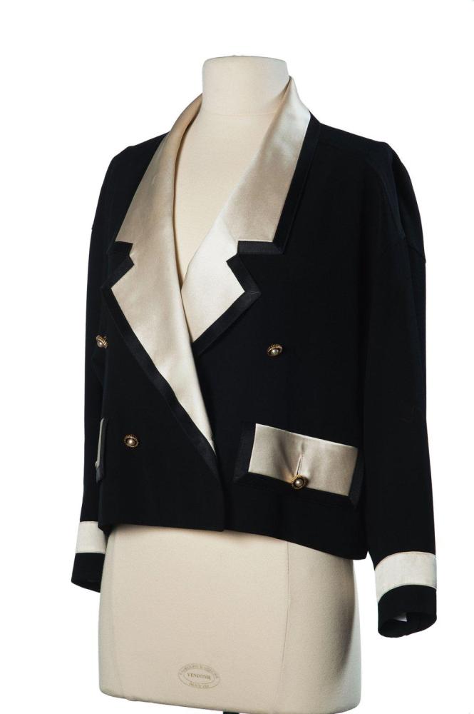 CHANEL

BOUTIQUE Spencer en crêpe de laine noire gansée de satin écru, noir, col châle cranté, double boutonnage, deux poches a rabat, rappel du satin au bas des manches longues, fentes au dos (taches, fils tirés, salissures)
