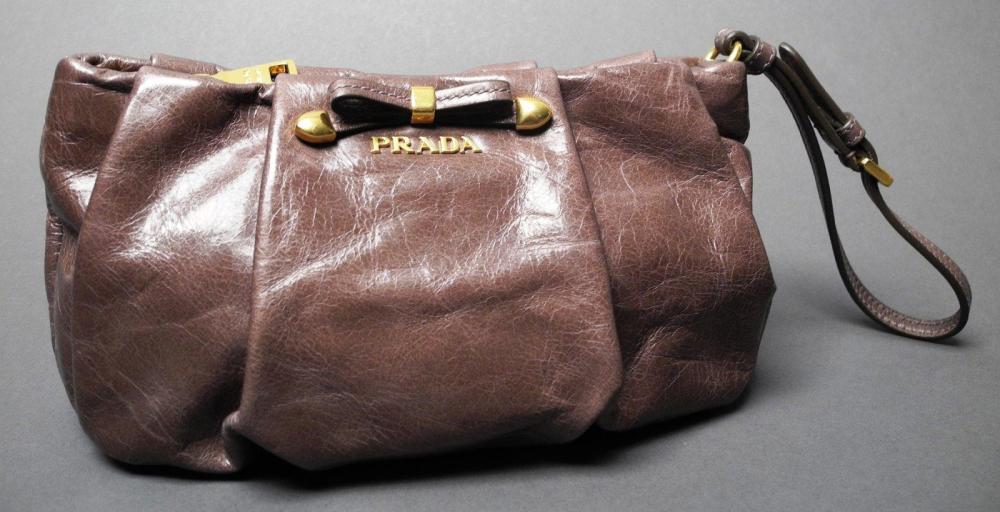 PRADA

Pochette en cuir marron plissé orné d’un noeud surmontant le sigle Garniture en métal doré Fermeture zippée Anse porté poignée réglable L: 20 cm ETAT NEUF Avec son dustbag et sa carte d’authenticité