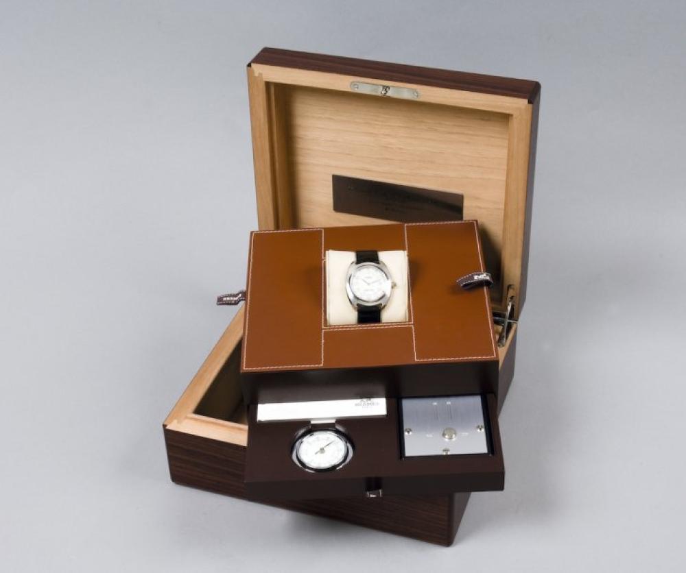 HERMÈS Paris made in France

série limitée n°16/75 2003 *Exceptionnelle montre d’Homme en platine «dressage» , mouvement P1928 mécanique à remontage automatique, cadran nacré, chiffres arabes, dateur à 3 heures, boucle déployante en or gris sur bracelet en crocodile noir, est présenté dans un coffret en cuir marron, rehausse d’une surpiqûre blanche figurant un H. Le coffret de présentation de la montre à un tiroir dans lequel se trouve un humidificateur et un hygromètre. L’ensemble est inséré dans un coffret à cigares en bois des îles, intérieur en cèdre, clef. L’ensemble a été réalisé pour le 75ème anniversaire de la montre Hermès