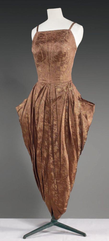 Emilio SCHUBERT Roma, circa 1948 / 1950

Robe de cocktail en broché marron, or, buste à fines bretelles sur décolleté carré, jupe fourreau agrémentée d’un tablier de forme tulipe à plis au dos et poches amphores de chaque côté, panneau rrondi partant de taille pour aller dans le dos. Sans griffe
