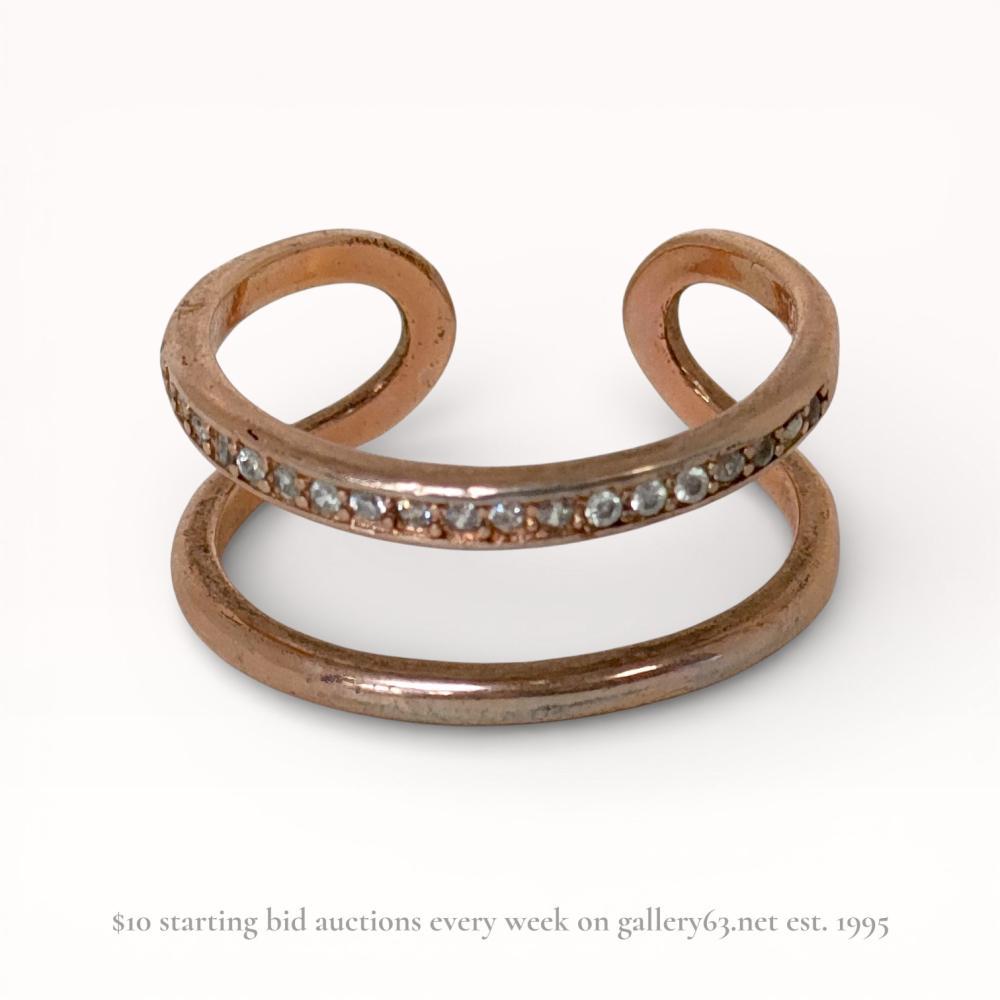 Description
Contemporary open-front cuff ring featuring a double-band design in rose gold-tone plated sterling silver. One band is channel-set with a row of approximately 20 small round faceted colorless stones. The interior is stamped S925, indicating a sterling silver base metal.
Size: US 7.