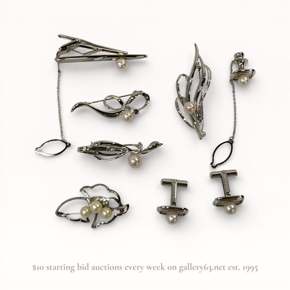 Description
An eight-piece collection of silver and cultured pearl jewelry, mid-20th century. The group includes four brooches with abstract leaf and ribbon motifs featuring rollover safety clasps, a pair of rectangular cufflinks, a matching tie tac, and a spring-loaded tie clip with safety chains. Each piece is set with white to cream cultured pearls and constructed from silver-toned metal marked SILVER and PAT P.