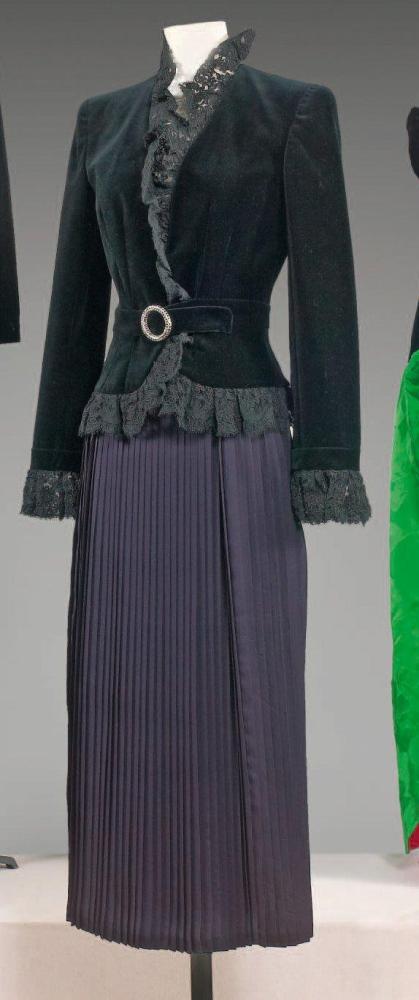 VALENTINO, circa 1985

Veste de cocktail en velours noir gansé de guipure de même couleur, encolure montante, effet de ceinture à boucle en métal argenté serti de strass façon diamants noirs, manches longues, se porte sur une jupe couture en mousseline plissée également noir. Griffes blanches, graphisme or, marron