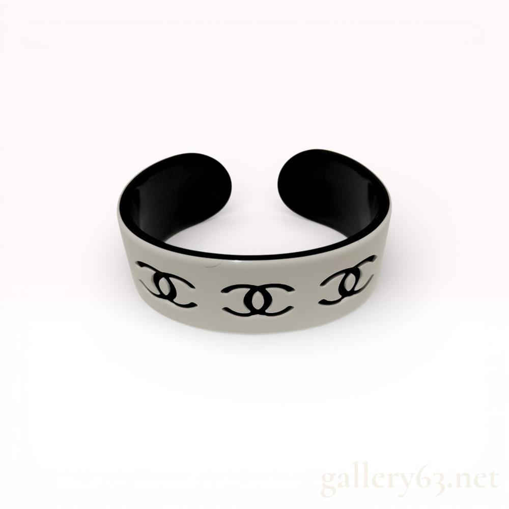 Description
Chanel monochrome resin cuff bracelet from the Spring 2002 collection. The wide, open-ended piece features a glossy white exterior with three inset black interlocking CC logos and a solid black interior. An oval authenticity plate is set into the interior bearing the mark (c)CHANEL(r) / 02 P / MADE IN FRANCE.