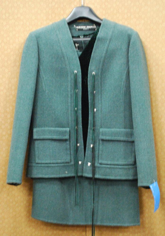 OGNIBEN ZENDMAN Roma, circa 1975

Tailleur en lainage à chevrons gris et vert sapin, veste à décolleté en pointe, sans col, parementure bord à bord à crochets métalliques, deux poches plaquées à rabat, manches longues, jupe légèrement évasé. Se porte avec un haut en velours tâcheté vert, décolleté en V, sans manches Griffe noire, graphisme blanc