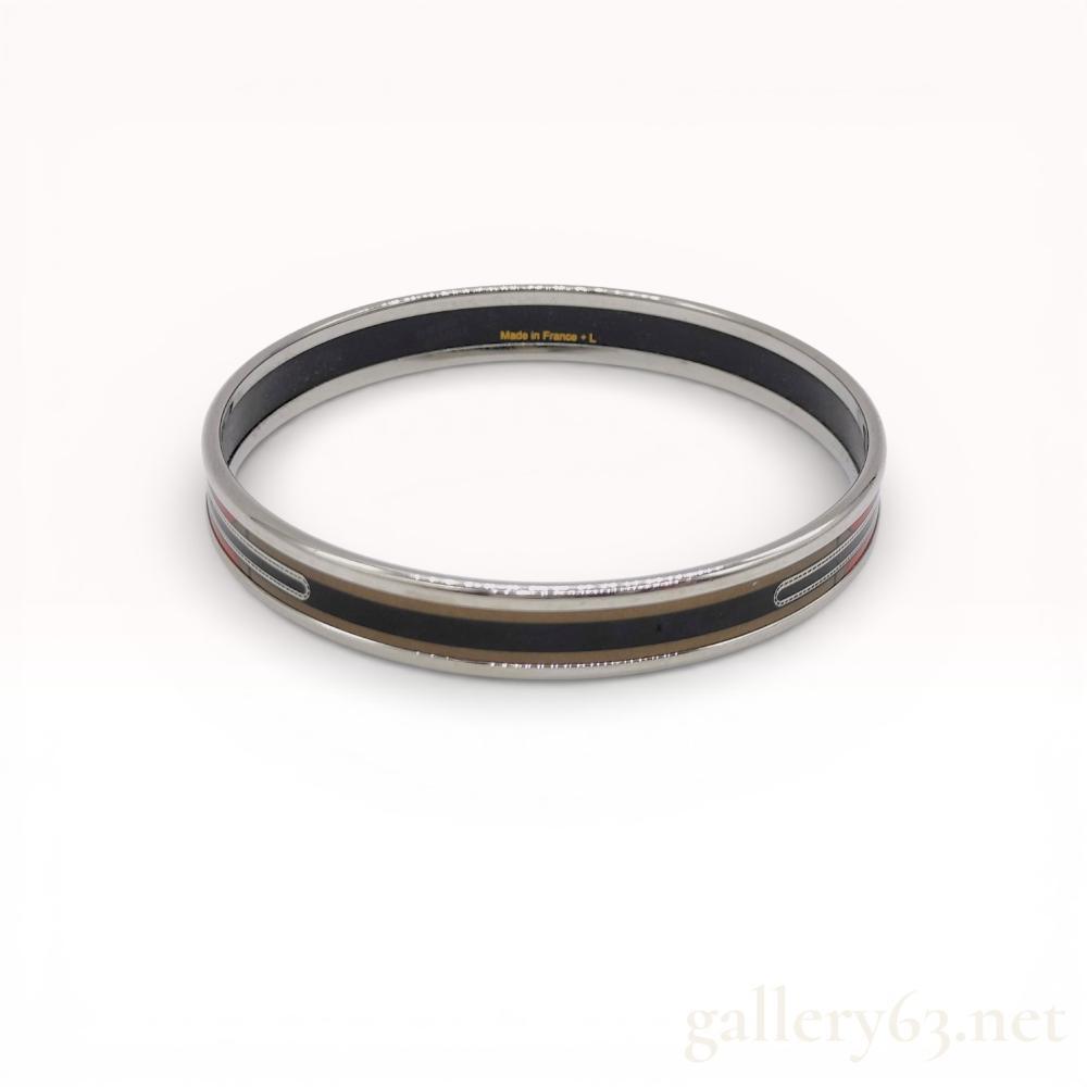 Description
Hermes narrow enamel bangle bracelet in a belt and buckle motif, late 20th century. Palladium-plated metal construction with a printed enamel inlay in red, black, and gold tones. Interior is marked Made in France + L and HERMES PARIS, while the exterior band is marked HERMES-PARIS.
Interior diameter: 6.5 cm
Exterior diameter: 7 cm
Width: 1 cm.