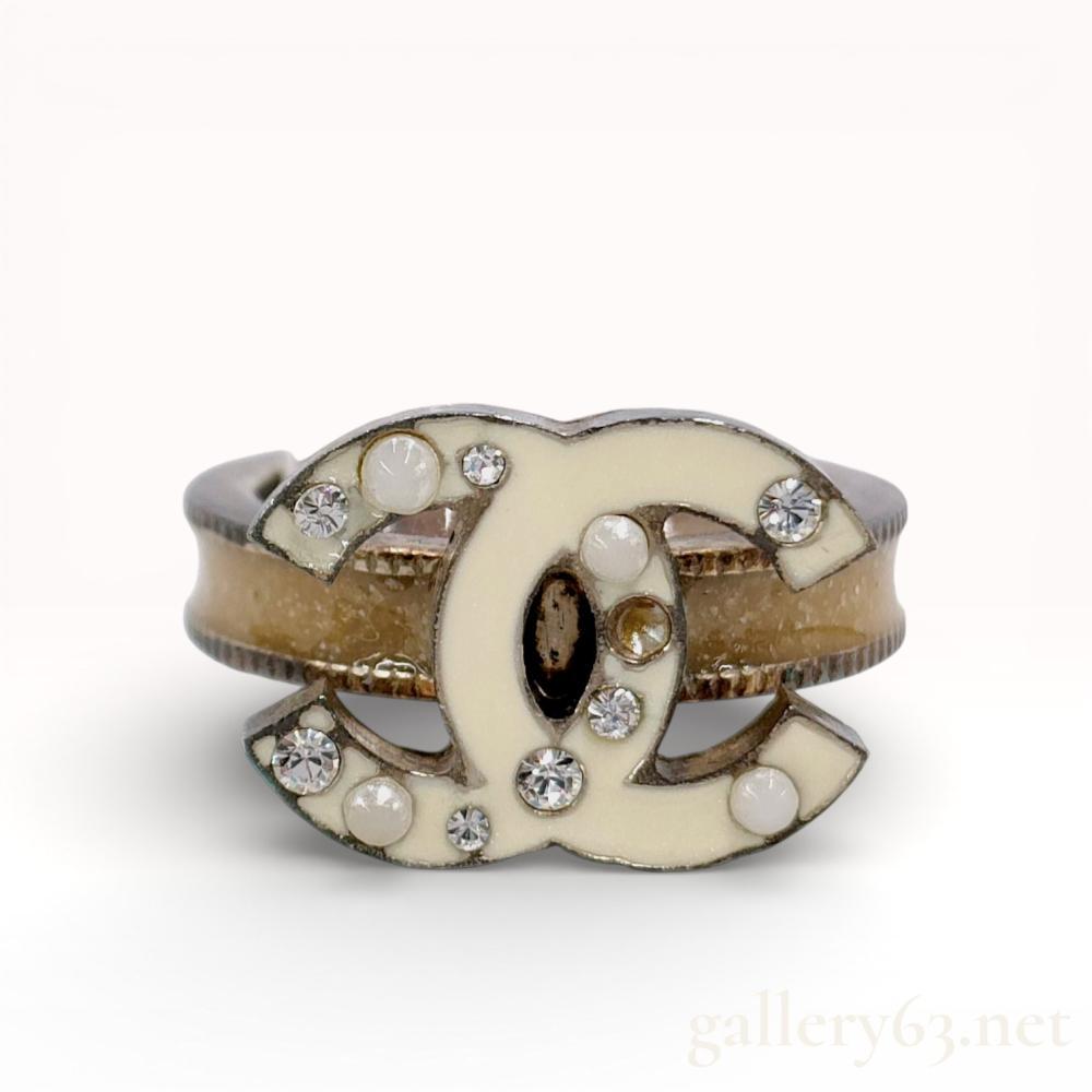 Description
Chanel interlocking CC logo statement ring from the Autumn 2007 collection. The base metal logo features cream enamel inlay set with clear faceted crystals and white cabochon faux pearls, while the band contains a tan resin channel between milled edges. An oval plaque on the reverse is marked Chanel 07 A Made in France. Includes original branded box.
Size: US size 11.