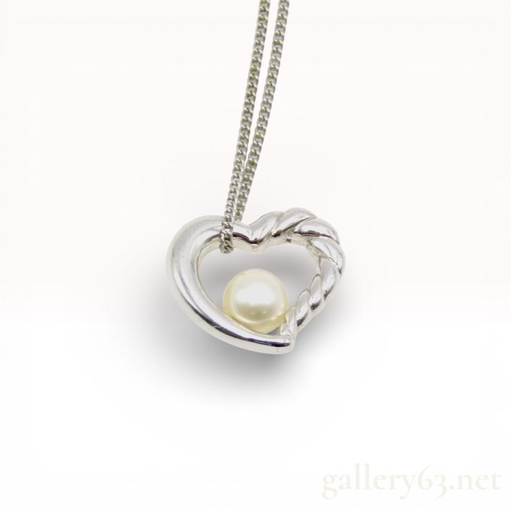 Description
Mikimoto sterling silver and cultured pearl necklace. The open-heart pendant features a dual-texture design with polished and twisted rope finishes, set with a single round white cultured pearl approximately 6.5mm in diameter. Suspended from a fine curb link chain with a spring ring clasp, the reverse of the pendant bears the Mikimoto M hallmark in a scalloped circle and an S sterling mark.