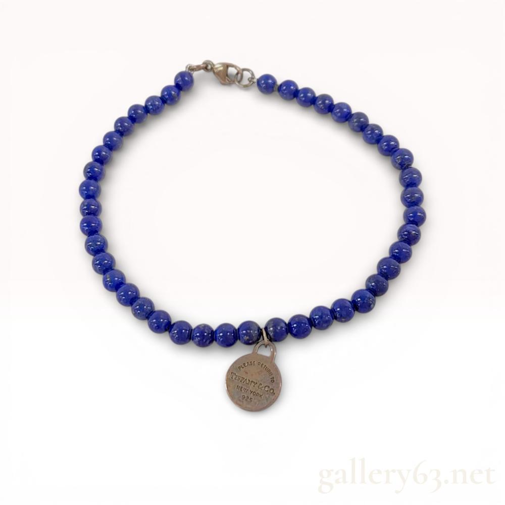 Description

A sterling silver beaded bracelet by Tiffany & Co. featuring a single strand of approximately 4mm round lapis lazuli beads. The stones exhibit a deep ultramarine blue color with characteristic golden pyrite inclusions. The bracelet features a circular Return to Tiffany tag engraved PLEASE RETURN TO TIFFANY & CO. NEW YORK 925 on the obverse and hallmarked © T&Co. 925 on the reverse. The piece is finished with a sterling silver lobster claw clasp and includes the original signature blue box and suede-finish drawstring pouch. Length: approximately 6.7 inches.





The Tiffany & Co. Lapis Lazuli Bead Bracelet from the ’Return to Tiffany’ series is a piece with layered meaning: the lapis lazuli, one of the most ancient and historically significant gemstones in human decorative history, paired with the house’s most recognizable identity marker. Lapis is the stone of Egyptian pharaohs, of Renaissance ultramarine pigment, of the night sky - its appearance in a Tiffany bracelet connects the house’s American heritage to civilizational antiquity. Return to Tiffany lapis pieces are rarer than the standard silver examples.