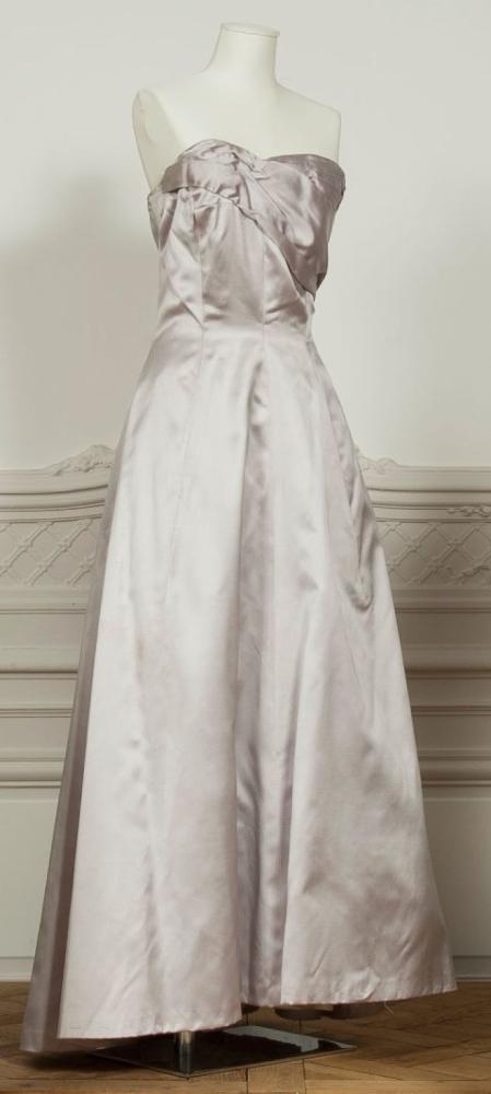 Jacques FATH Haute-Couture circa 1953/ 1955

Robe du soir de forme longue en satin parme, haut bustier souligné d’un drapé asymétrique, jupe princesse. (accident à la doublure, taches, fils tirés) Griffe blanche, graphisme noir rehaussé du sigle