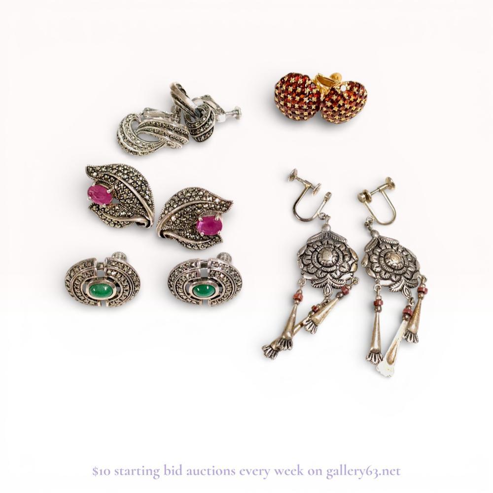 Description

A collection of five pairs of vintage earrings featuring sterling silver and marcasite, mid-20th century. The group includes gilt sterling silver garnet pave dome earrings, marcasite-set scroll and leaf motifs, circular sterling silver earrings with green cabochons, and Turkish-style chandelier drop earrings with red beads. Construction includes screw-back and clip-on mechanisms, with 925 hallmarks and stylized maker’s marks visible on the reverse of the mountings, including a 925 in an oval and a 925.
Measurements range from approximately 1.5 centimeters to 6 centimeters in length.

57.2 grams.