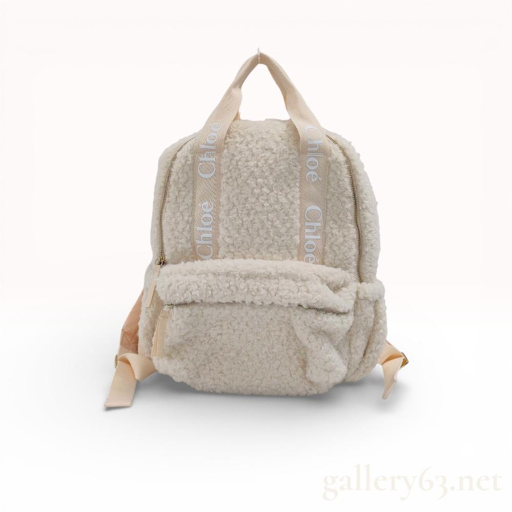 Description
Chloe Woody backpack crafted from cream faux shearling fleece and canvas. It features signature logo-printed canvas top handles and shoulder straps, a main zippered compartment, and a front zippered pocket. The back panel and interior are lined with a peach-colored synthetic textile, accented by gold-tone hardware and an interior embossed leather logo patch.
Approximately 12 inches height by 10 inches width.
