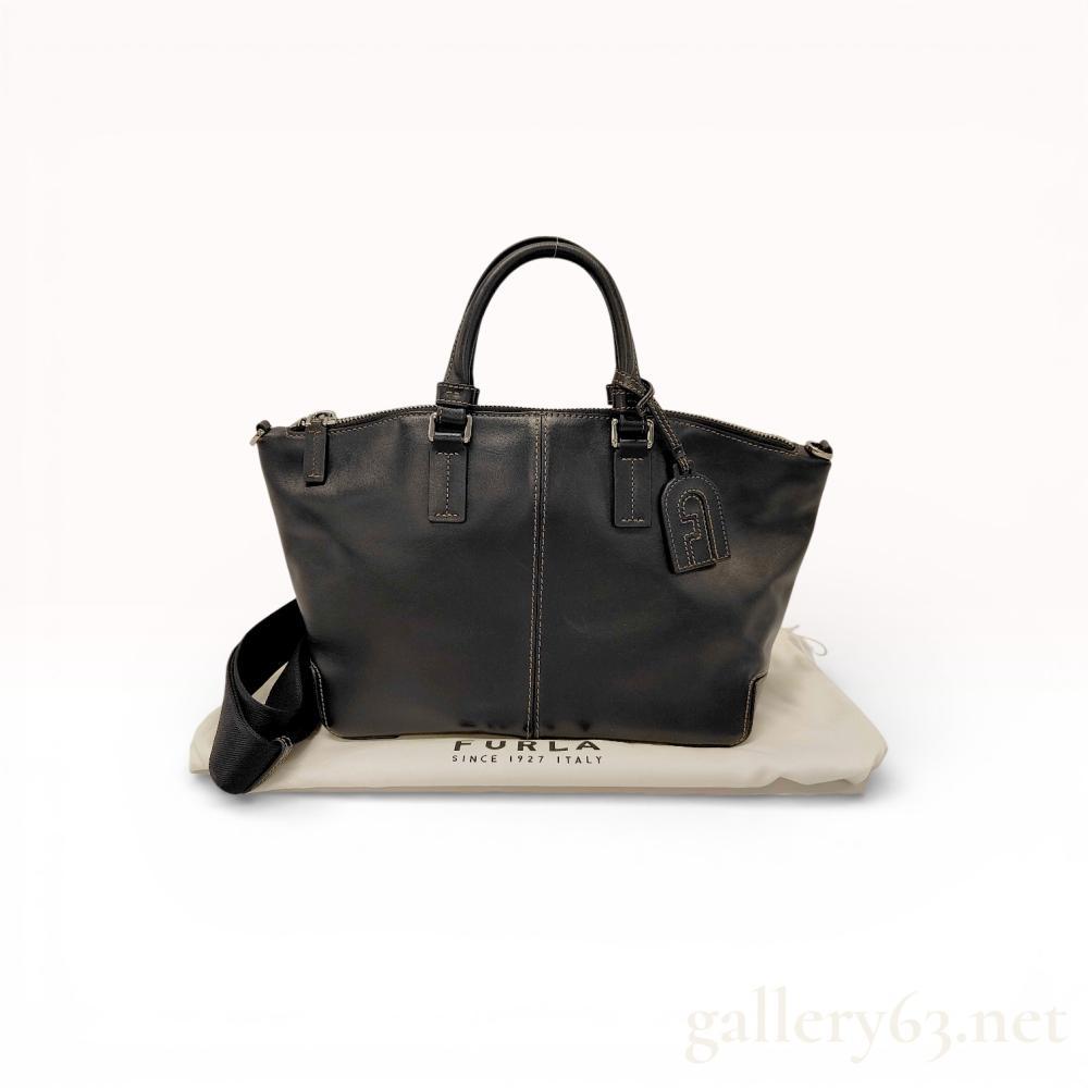 Description
Authentic Furla Sirio tote bag in balck smooth leather, featuring a structured trapezoidal silhouette with contrast topstitching and center seam detail. The design includes dual rolled top handles with silver tone hardware and a hanging leather tag. A detachable wide shoulder strap allows for crossbody or shoulder carry. Includes dust bag.