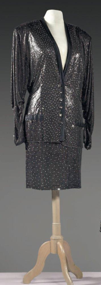 Gianni VERSACE

Tailleur en cotte de maille noire parsemée de strass composé d’une veste de forme gilet gansée de soie polyester, effet de simple boutonnage, manches longues drapées, deux fausses poches, et d’une jupe droite. (petits trous) Griffe noire, graphisme blanc, or