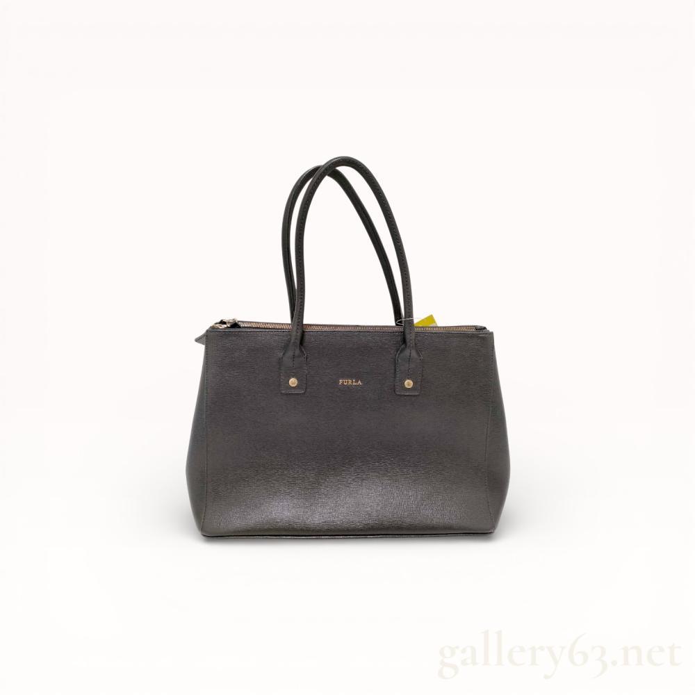 Description
Furla Linda tote crafted from black Saffiano leather with a structured trapezoidal silhouette and dual rolled top handles. The exterior features gold-tone hardware including front logo lettering, engraved handle studs, and four protective base feet. The interior is organized into three compartments with a central zippered section and two open sections secured by magnetic snaps.
Width: 14 inches
Height: 10 inches
Depth: 6 inches.