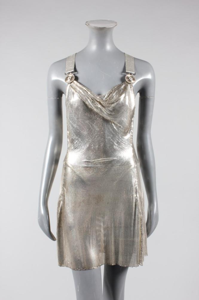 

A fine Gianni Versace silver-mesh cocktail dress, Autumn-Winter, 1994-95, with diamond Atelier label, with rhinestone studded silvered Medusa-head clips and Y-shaped silver top-stitched straps, with draped cowl to front of bodice, integral silver lycra body, i bust 86cm, 34in, waist 66cm, 26in



Versace used metal mesh in his designs from the 1980s onwards. These progressed from boxy rectangular shapes in the early collections to neo-classical drapery by the 1990s, suggestive of female gladiators. This fine metal mesh produced a molten, almost wet-look effect, which in combination with silver or gold tones produced the glamorous ’bling’ effect for which he was renowned.
