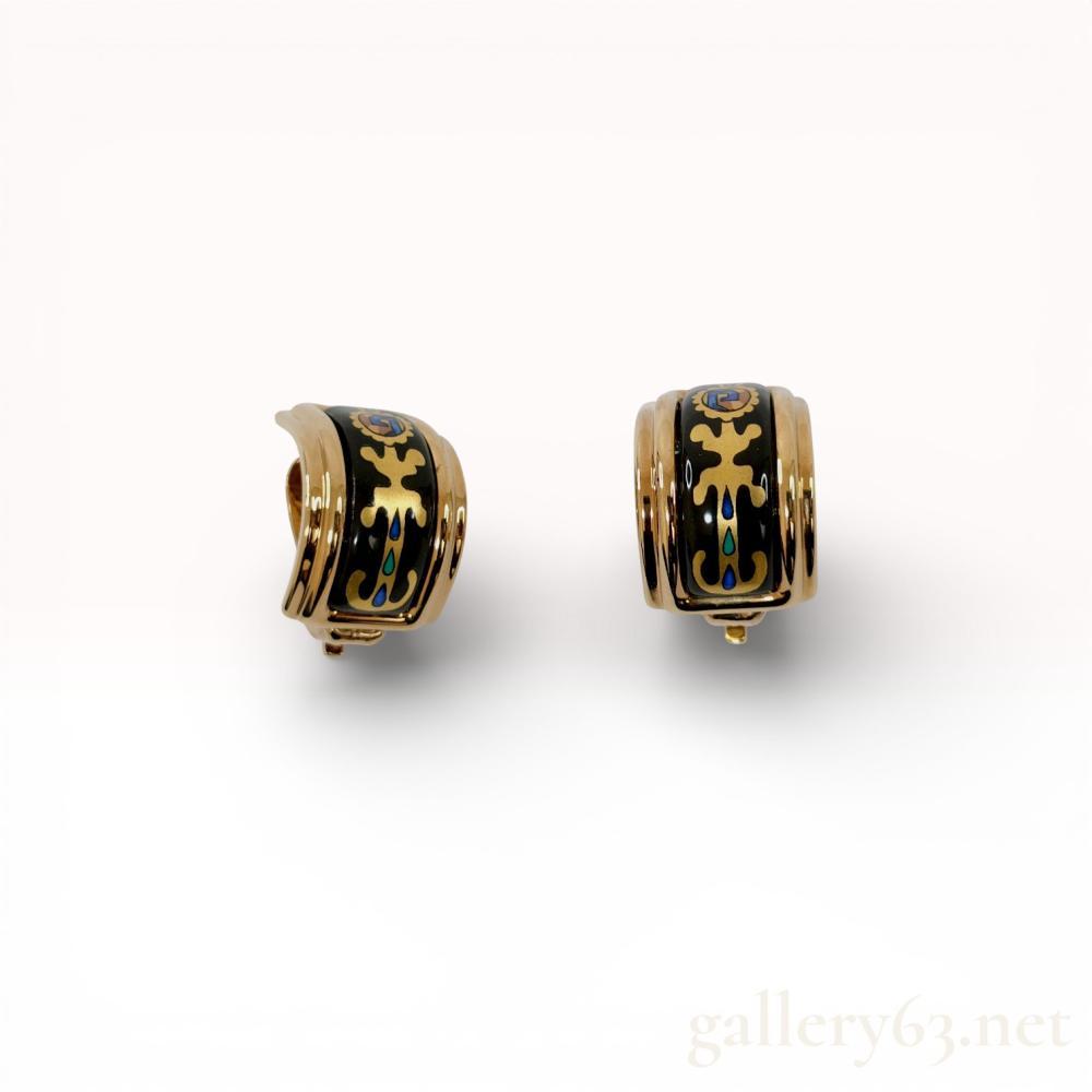 Description
A matched pair of Hermes C-hoop earrings featuring black enamel inlays with stylized foliate patterns. The gold-tone metal frames house central panels decorated with scrolling gold-tone motifs and small blue and green enamel accents. Each earring is fitted with a hinged clip-on mechanism and includes a white circular comfort pad. The interior of each earring is stamped with the HERMES mark and a square hallmark.
Each measures approximately 20mm in height and 10mm in width.