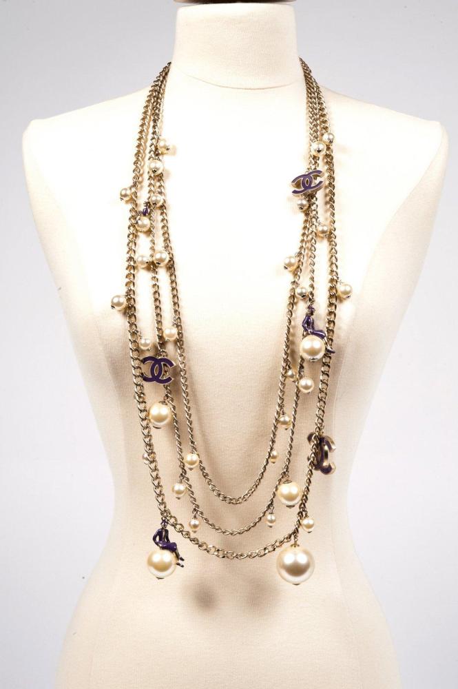 CHANEL CIRCA 2004

Sautoir composé de trois chaînes en métal argenté ornées de perles blanches de tailles différentes, certaines à l’effigie de Mademoiselle émaillée assise, et rehaussées du sigle émaillé violet. Signé, daté