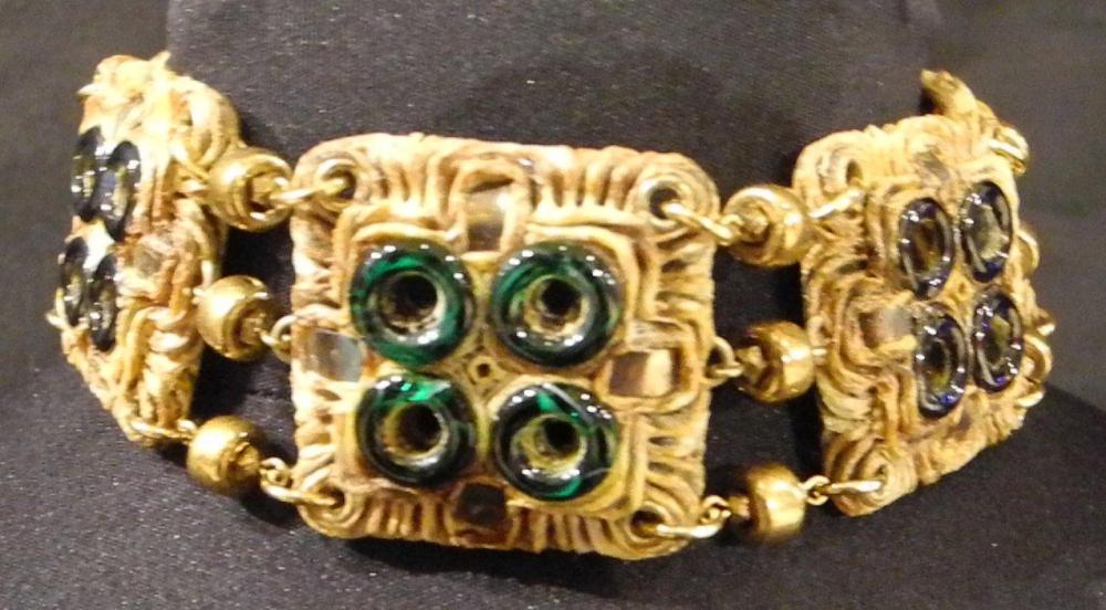 HENRY - circa 1960

Collier ras-du-cou composé d’éléments carrés en résine gravée rehaussés de disques en pâte de verre verte et bleue monté sur une chaîne en métal doré Signé au revers des éléments