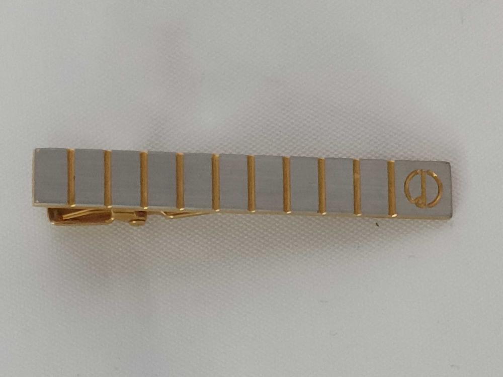 Description
Christian Dior two-tone metal tie clip, late 20th century. The rectangular bar features brushed silver-toned panels separated by recessed gold-toned vertical bands and a circular field with an incised interlaced CD logo. The reverse is fitted with a gold-toned spring-loaded alligator tension clip and bears illegible recessed marks.
Approximately 52 mm in length.