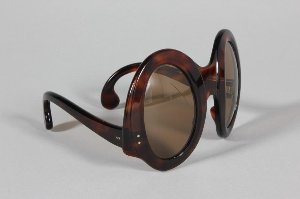 

A pair of Philippe Chevalier sunglasses, late 60s-early 70s, with faux tortoiseshell frames, sloping oval lenses and arms with curved comma tips, 15cm wide
