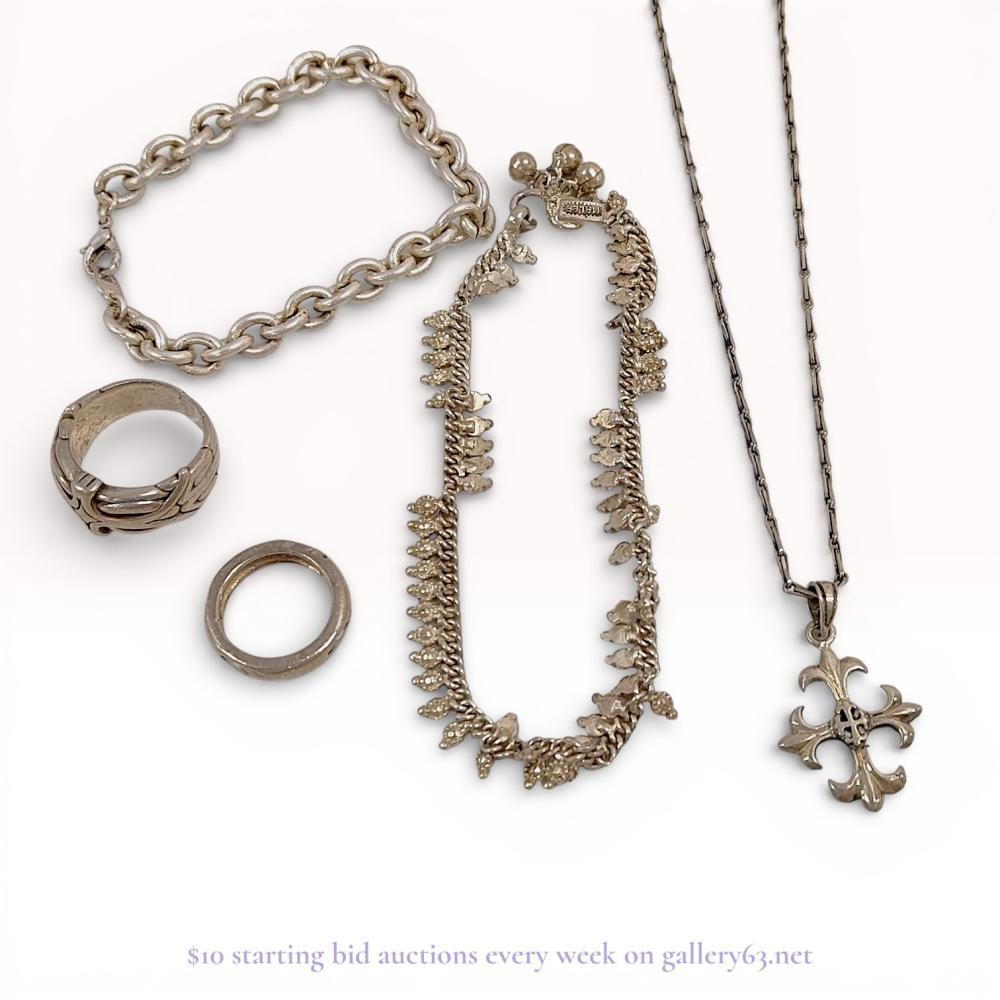 Description
Malee charm necklace and a collection of sterling silver jewelry. The lot features a heavy sterling silver rolo-link chain bracelet with a lobster claw clasp and a 925 fineness mark, a bar-link chain necklace with a fleur-de-lis cross pendant featuring a dark center inset, and a decorative choker-style charm necklace with bell terminals. Two silver  band rings are included, one with an ornate relief scroll pattern and one with a simple polished finish. Notable marks include the Malee maker mark under a stylized peak motif on a rectangular plaque and a 925 stamp on the bracelet jump ring. 68 grams.