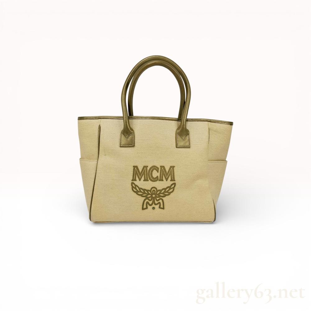 Description
MCM tote bag in beige woven canvas featuring a large embroidered olive-gold logo and laurel wreath on the front. The exterior includes dual rolled metallic gold-tone leather handles, a front zippered pocket, and side slip pockets. The interior is lined with tan ribbed grosgrain fabric and contains one zippered pocket.
Base Width: 11 inches
Height: 10 inches
Depth: 6 inches.