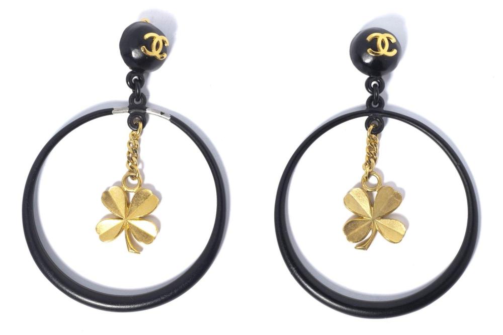 CHANEL

Paire de créoles en composite et métal émaillé noir figurant un bouton siglé, un anneau rehaussé d’un trèfle en pendentif. (manque une raquette) Signée
