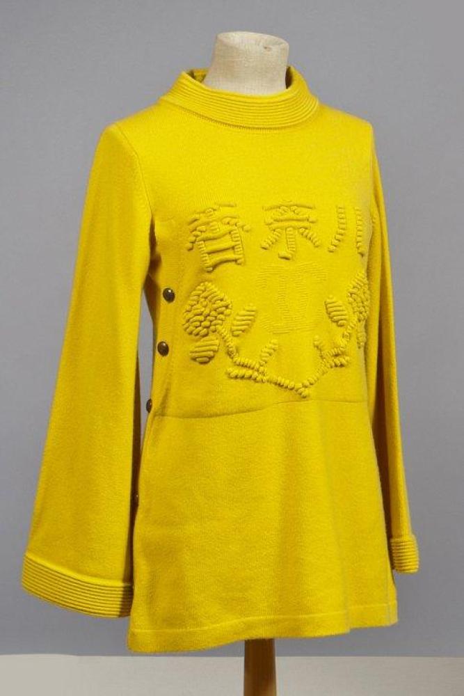 CHANEL

Robe en cachemire bouton d’or d’inspiration chinoise, encolure decollée soulignée de petits boudins, buste agrementé d’écritures en relief et du sigle tricoté dans la maille, côtés boutonnés, manches longues à poignets larges avec rappel des nervures