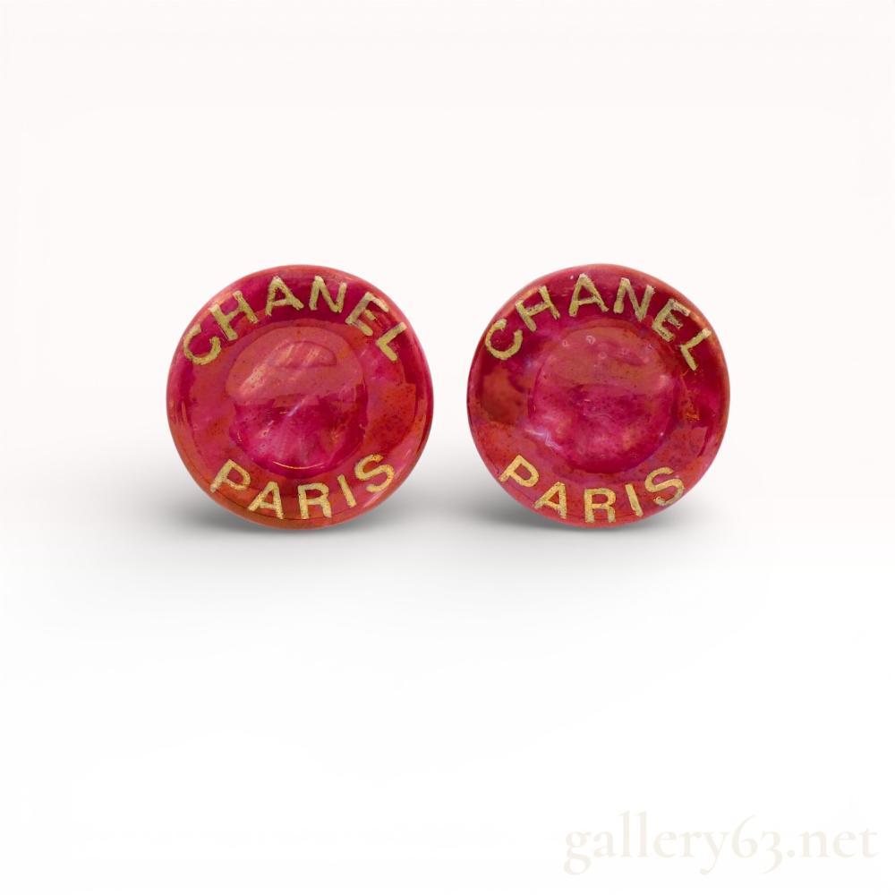 Description
Chanel button-style clip-on earrings from the Spring 1997 collection. Each earring features a domed circular front with a mottled deep pink finish and raised gold-tone lettering reading CHANEL PARIS. The reverse is finished with gold-tone metal backings, functional clip mechanisms, and stamped oval plates reading CHANEL 97 P MADE IN FRANCE. Includes a black Chanel presentation box with white branded ribbon.
