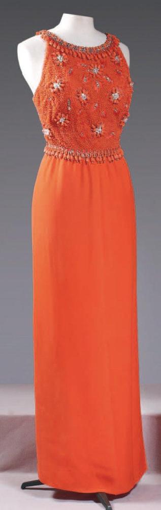 BUONANNO, circa 1960

Robe longue en crêpe corail, haut en tulle de même couleur rebrodé de perles, de strass, de fils de soie finissant en pampilles, encolure bateau sans manches sur dos nu, sur une jupe fluide fendue sur le devant. (petits manques) Griffe blanche, graphisme noir