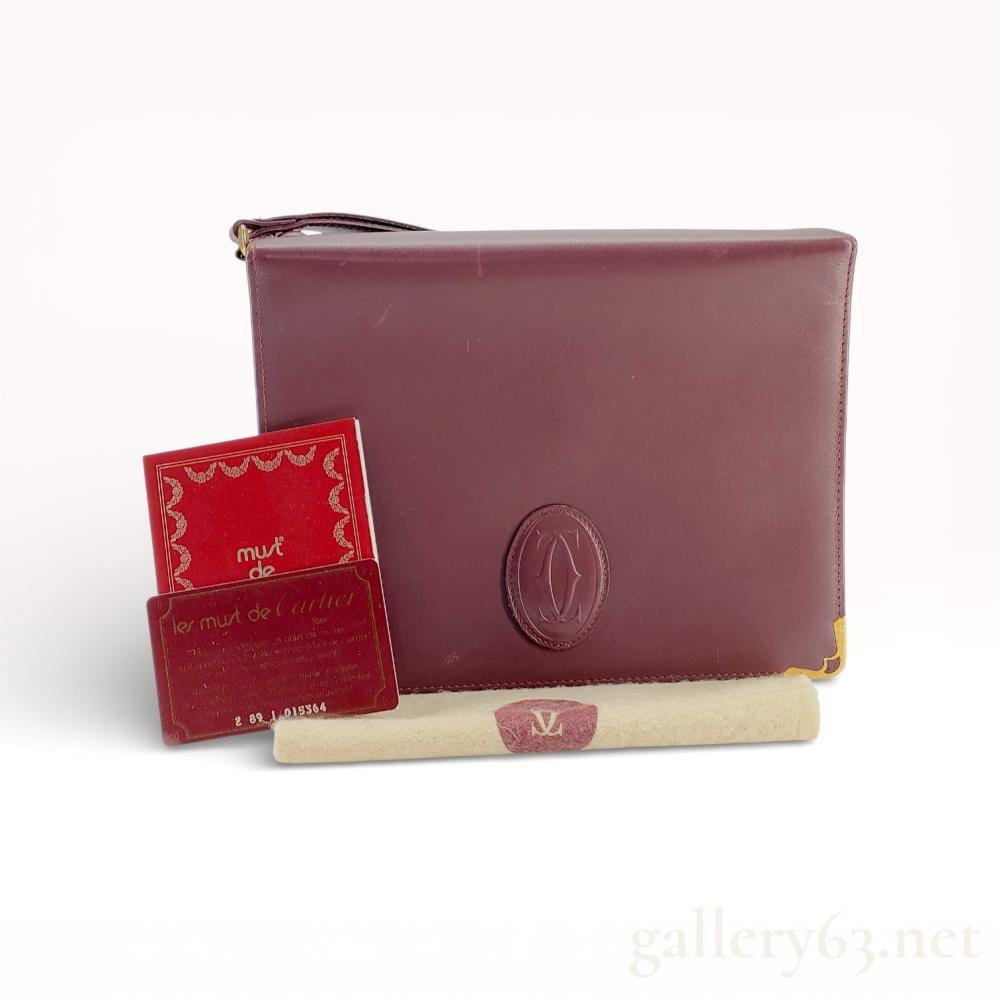 Description
Cartier Must de Cartier vintage envelope clutch bag in signature bordeaux smooth leather. The exterior features a centrally embossed interlocking C logo, gold-tone metal corner protectors, and an integrated leather wristlet strap. The interior is organized with accordion compartments, a zippered security pocket, and a secondary snap-closure pocket. Accompanied by an authenticity card numbered 2 89 1 015364, a brand booklet, and a logo-stamped protective felt strip.
Width: Approximately 10 inches.
