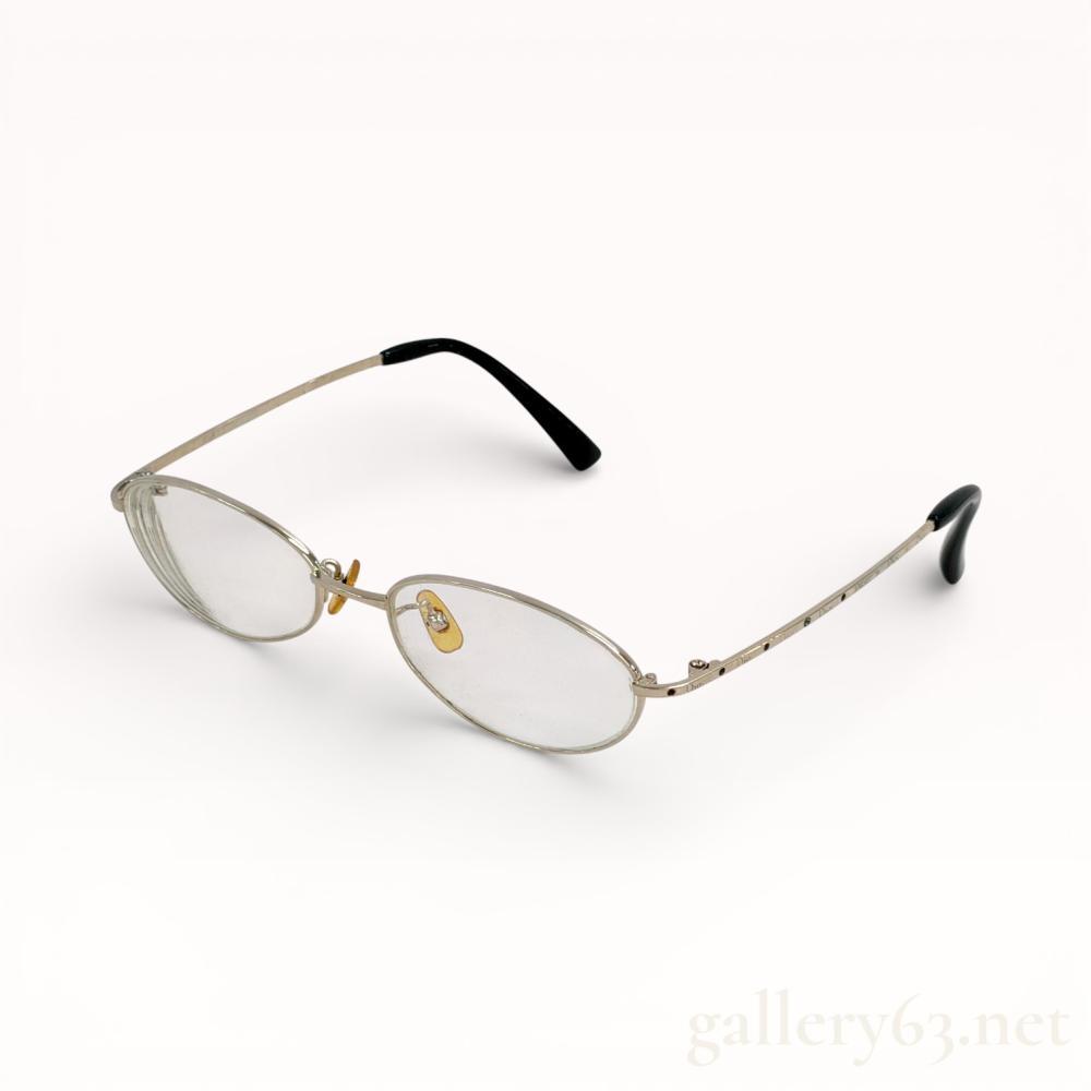 Description
Authentic Dior eyeglasses featuring oval clear lenses set within a slim metal frame. Frame presenting a light gold-tone finish with adjustable nose pads and fine etched detailing along the temples. Temples fitted with black curved ear tips for comfort and stability. Design presenting a lightweight, minimalist profile consistent with Dior eyewear.