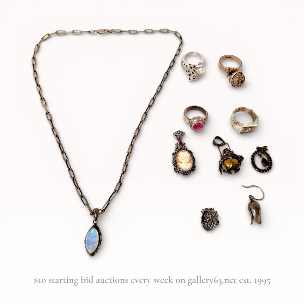 Description
This collection features a sterling silver necklace with a marquise moonstone cabochon and a rectangular-link chain. Included are four rings: a panther bypass ring with a cultured pearl, a signet ring marked SILVER with the character for Love, a pink cabochon ring, and a filigree sphere ring. The lot also contains three pendants including a shell cameo with marcasites and garnets, a garnet cluster pendant, and a cage pendant, alongside a marcasite beetle component and a single flower bud earring. The necklace and moonstone pendant are marked 925. 78 grams