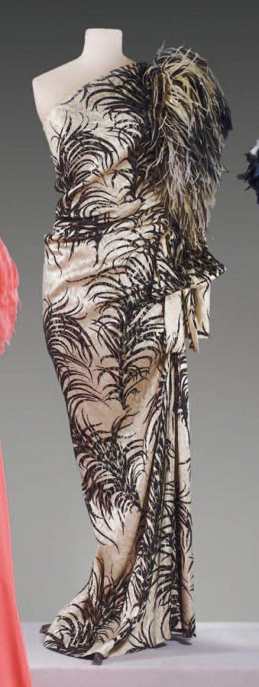 GIVENCHY

Robe du soir en soie lamée longue à motifs d’herbes de savane noires sur fond beige, or, décolleté asymétrique à une manches ornée à l’épaule de plumes de marabout auc couleurs, juoe droite àç effet de drpapé sur un côté agrémenté d’un noeud. (ourlet non d’origine) Travail de couturière