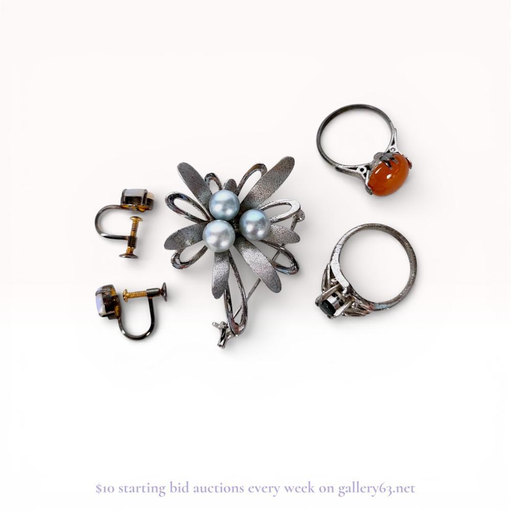 Description
An assortment of vintage jewelry featuring a sterling silver floral brooch, a pair of screw-back earrings, and two rings. The brooch is designed with textured petals and three light blue spherical beads, bearing a 925 mark on the reverse. The earrings contain oval opal cabochons in silver-tone settings with gold-tone screw-back mechanisms, and the rings are set with a dark round-cut stone and an orange-brown cabochon.
Brooch: 1.5 inches diameter
Earrings: 0.4 inches length.