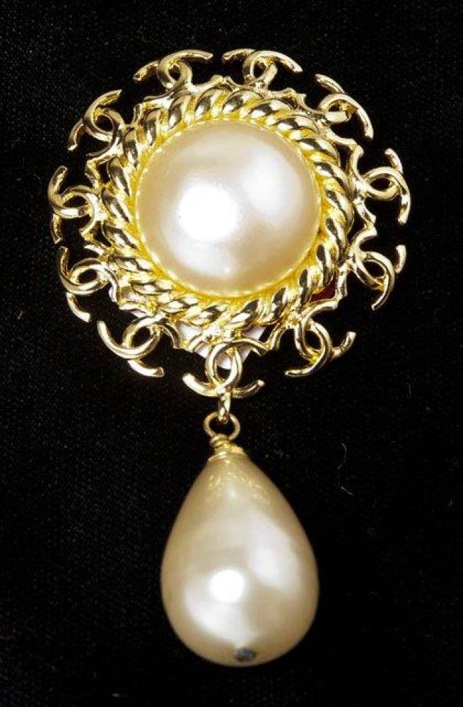 CHANEL, circa 1997

Broche en métal doré repercé du sigle ornée au dentre d’une demi perle soutenant une goutte. Signée