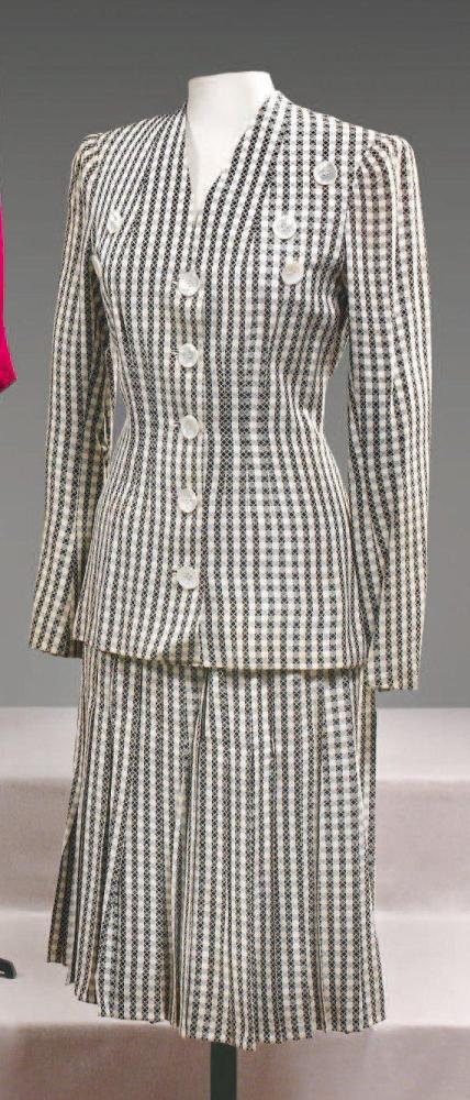 Marcel ROCHAS

Tailleur en reps de soie à carreaux noir, blanc superposé d’un motif croisillon écru, veste longue à encolure en V soulignée de boutons cousus en asymétrie annonçant le simple boutonnage, jupe plissée à partir des petites hanches. (manque une garniture à l’encolure, taches ) Griffe marine, graphisme blanc, rouge