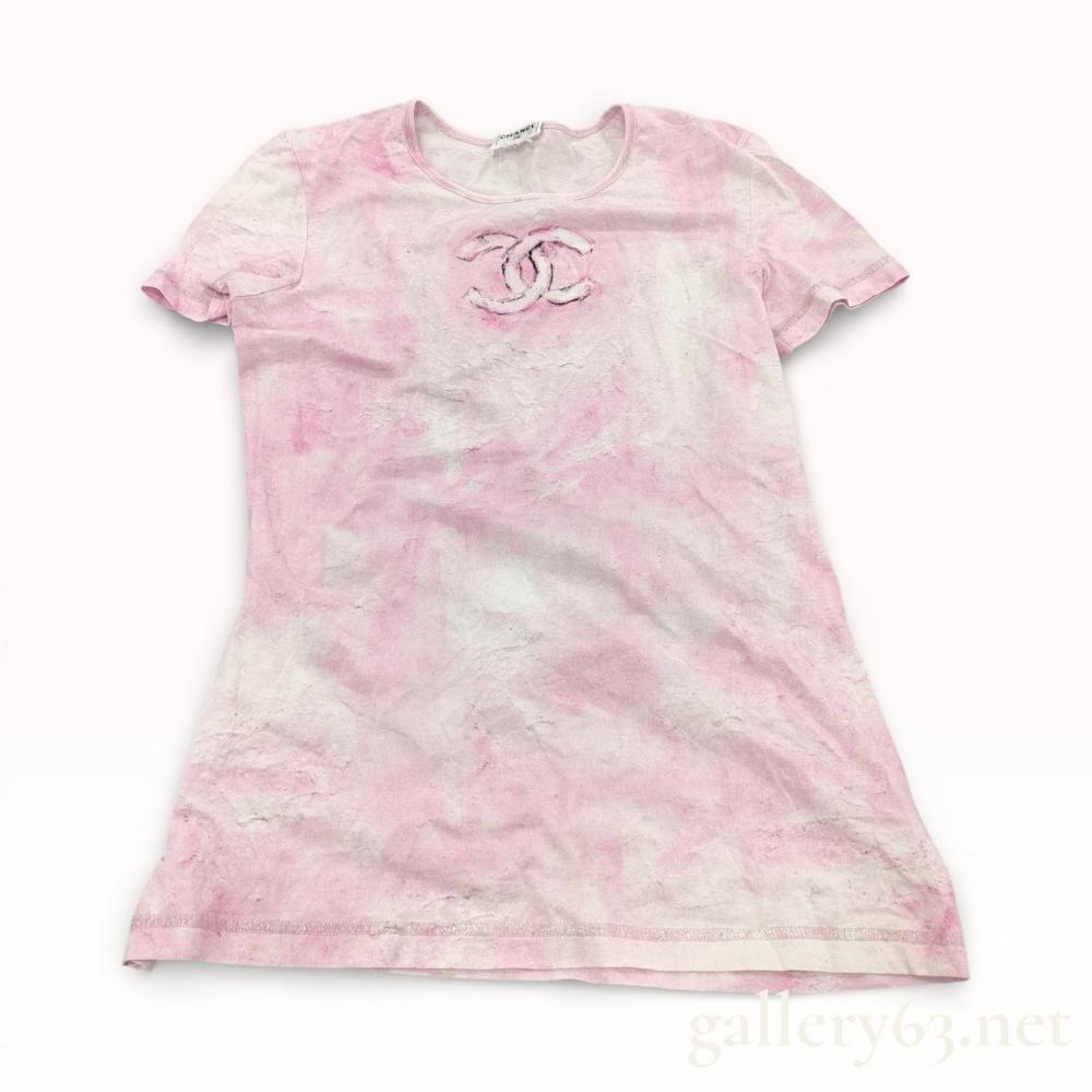 Description
Chanel short-sleeved crew-neck t-shirt featuring a pink and white marbleized tie-dye pattern. The center chest is decorated with a large interlocking CC logo in a distressed painterly aesthetic with dark purple accents. This cotton jersey garment is finished with tonal pink and metallic silver-tone topstitching at the neckline, sleeve cuffs, and hem. An interior woven neck label is present, marked CHANEL with a circled interlocking CC logo.
Length: 23.5 inches.