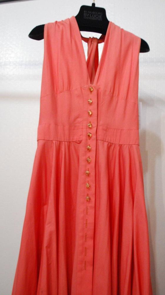 Anonyme

Robe en coton saumon, encolure américaine sur échancrure et sur dos nu d’où se croisent des bretelles, boutonnage en bakélite jusqu’à la fente de la jupe très ample