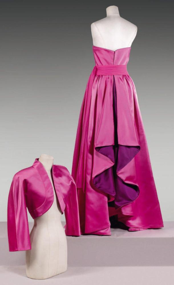 Mila SCHON, circa 1978 / 1980

Robe grand soir en satin de soie fuchsia, haut à double bustier agrémenté de satin violet se prolongeant au dos sur la jupe ample par deux panneaux découpés ; taille froncée soulignée d’une ceinture de mousseline drapée à deux pans, se porte sous boléro à encolure montante, parementures arrondies, manches longues raglan. Griffe blanche, graphisme noir