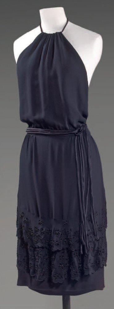 VALENTINO, circa 1990

Robe de cocktail en crêpe de soie noir, encolure américaine sur dos nu, taille soulignée de liens de même tissu, jupe très souple sur deux niveaux rebrodés de perles de jais à motif floral redécoupé donnant l’illusion d’une broderie anglaise. Griffe blanche, graphisme or