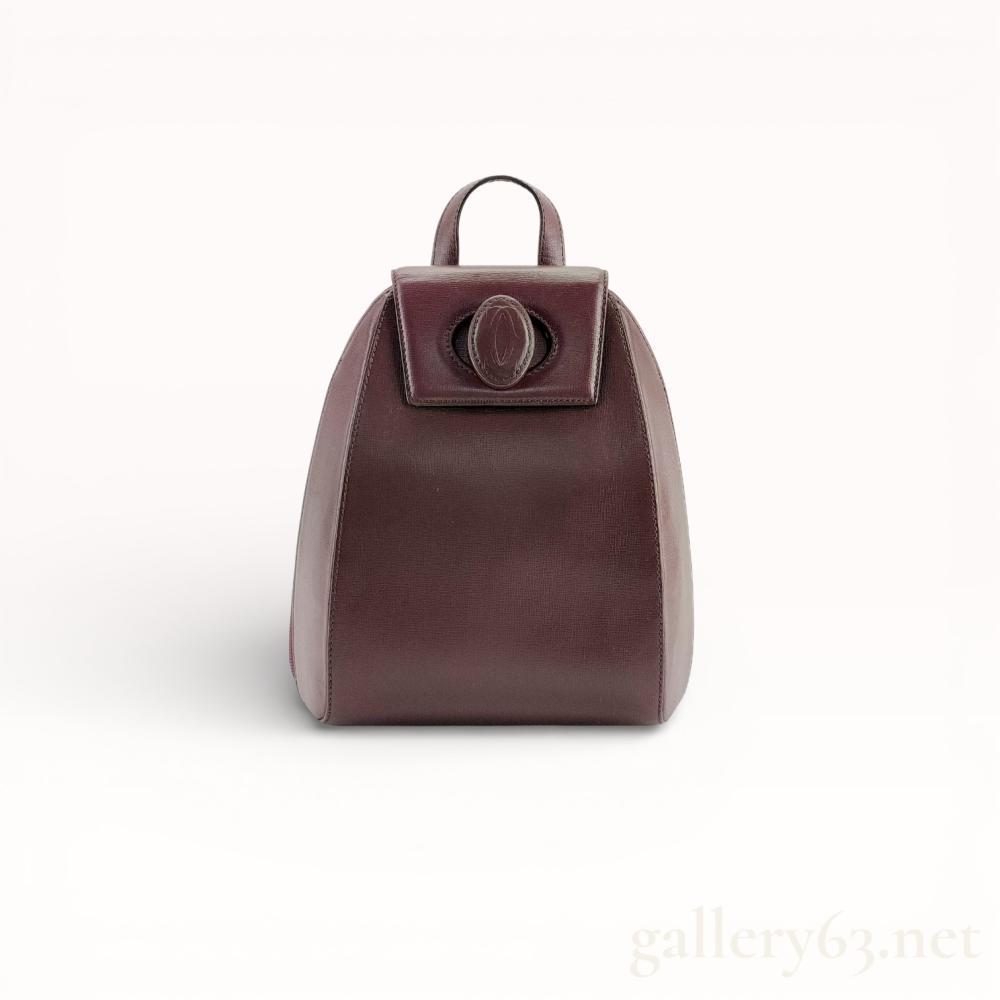 Description
A vintage Must de Cartier backpack crafted from signature bordeaux grained leather with gold-tone hardware. The tapered silhouette features a top flap with an embossed interlocking C logo medallion, a leather top handle, and adjustable shoulder straps. The interior is lined with a tonal jacquard fabric repeating the Cartier Paris motif and includes a top zip closure with dual leather pulls.
Approximately 10 inches in height.