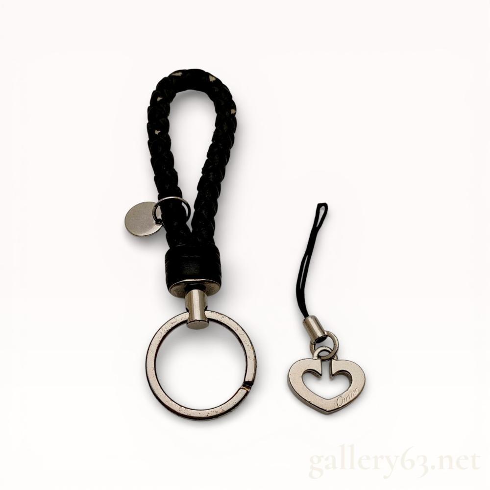 Description
A Cartier heart-motif charm strap and a black braided cord keychain, contemporary. The silver-toned metal charm features the signature C de Cartier heart design on a black cord, while the keychain consists of a black woven loop with a silver-toned split ring and circular tag. The heart charm is signed Cartier, and the lot is accompanied by an original red Cartier presentation box and black fabric pouch.
Braided Keychain: 4.25 inches total length
Heart Charm: 0.85 inches width; 3.15 inches total length.