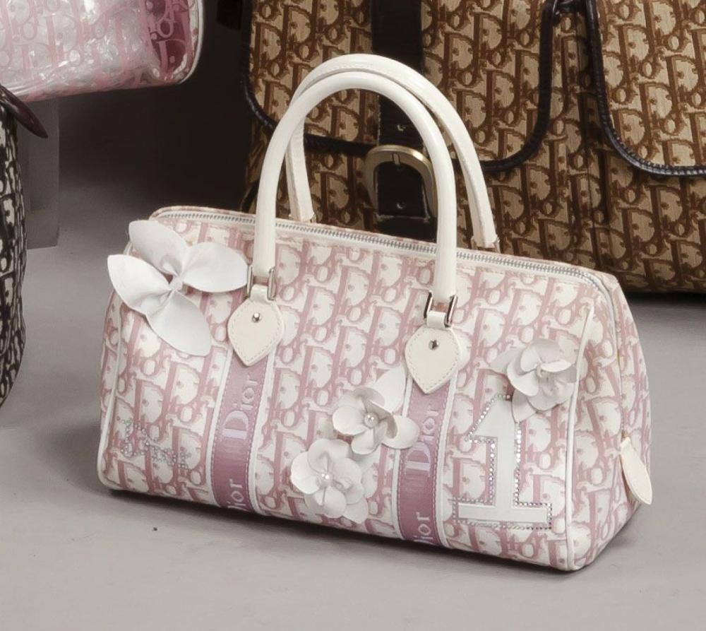 Christian DIOR

Sac en PVC siglé rose sur fond blanc, agrémenté de deux applications de sangles en coordonné, du chiffre" 1", de fleurettes blanches et de strass formant le non, fermeture éclair, double poignée. (Taches).