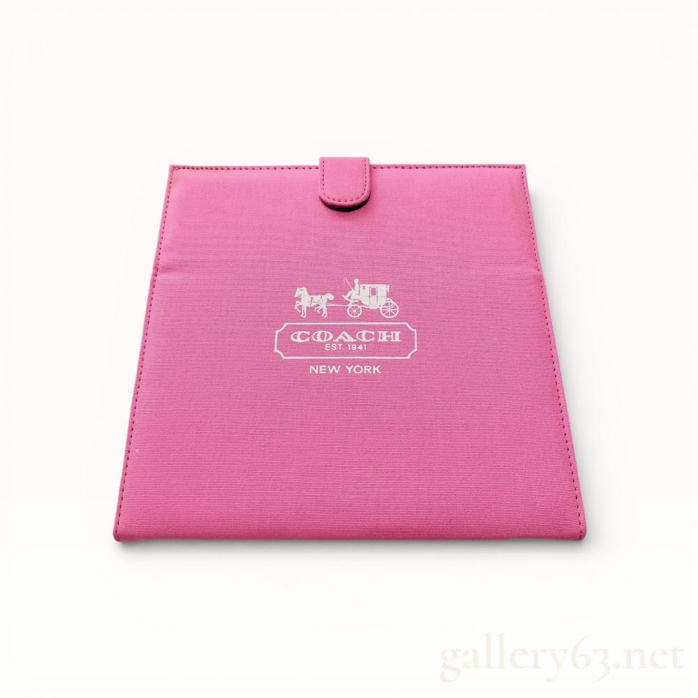 Description
Coach folding travel vanity mirror featuring a pink canvas exterior and a glass interior. The front displays the white printed horse and carriage logo with COACH EST. 1941 NEW YORK, while the reverse features a white dotted signature C pattern. It includes a tonal fabric-covered snap closure and is accompanied by its original pink presentation box.