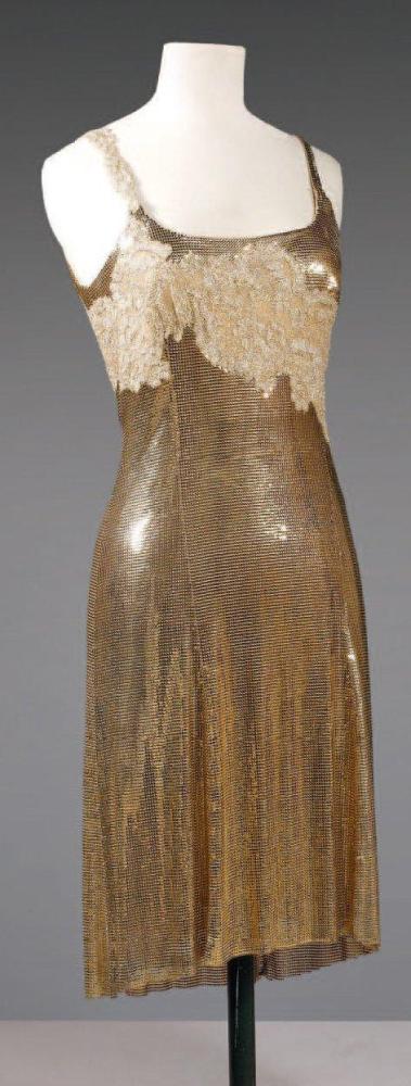 Gianni VERSACE

Robe de forme combinaison en cotte de maille or, décolleté bateau souligné d’une dentelle de résille or, dos et une bretelle à l’identique. Griffe noire, graphisme or, blanc