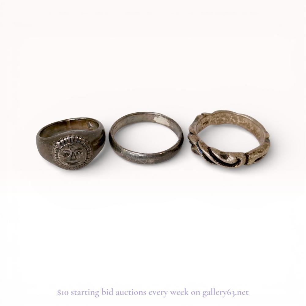 Description
A trio of white metal and sterling silver rings in various decorative styles. The set includes a signet-style ring featuring a celestial sun face with a radiating border, a simple rounded band stamped 925, and a decorative band with an intertwined rope design. The signet ring contains illegible marks on the interior, while the twisted band is unmarked.
Sun face ring: US size 8.5
Plain band: US size 10
Twisted band: US size 10.5.